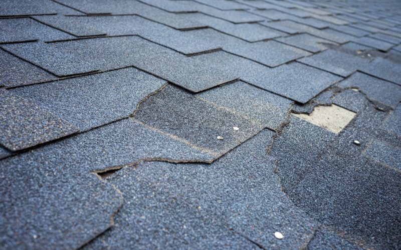 Сlose up view of bitumen shingles roof damage that needs repair.