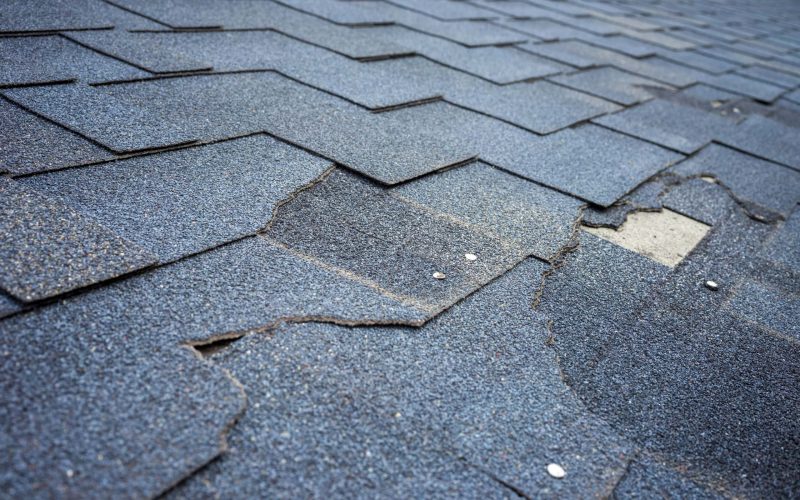 Сlose up view of bitumen shingles roof damage that needs repair.