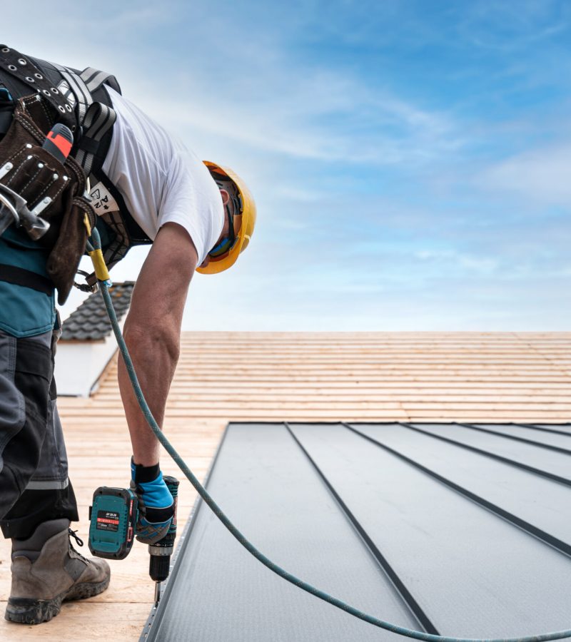 A roofer with a safety harness and tool belt is working with a e